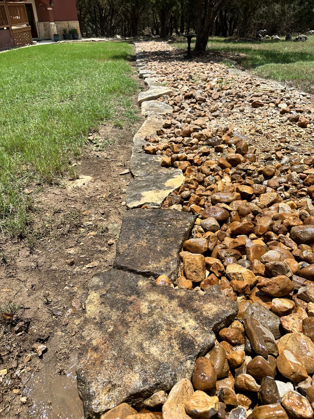 Natural stone path alongside a gravel drainage area in a grassy landscape.
