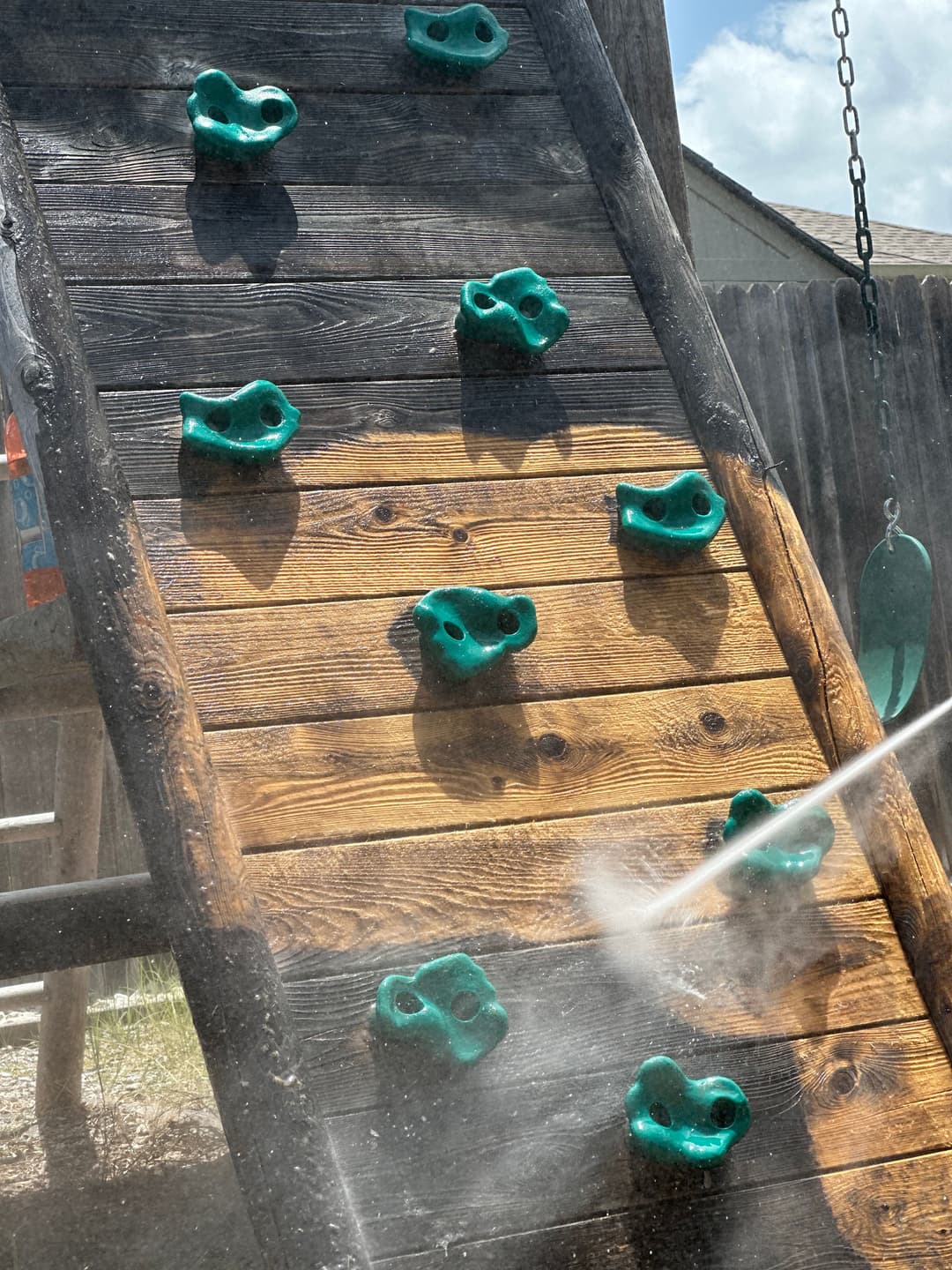 Colorful climbing wall with green rocks for kids on a wooden playground structure.