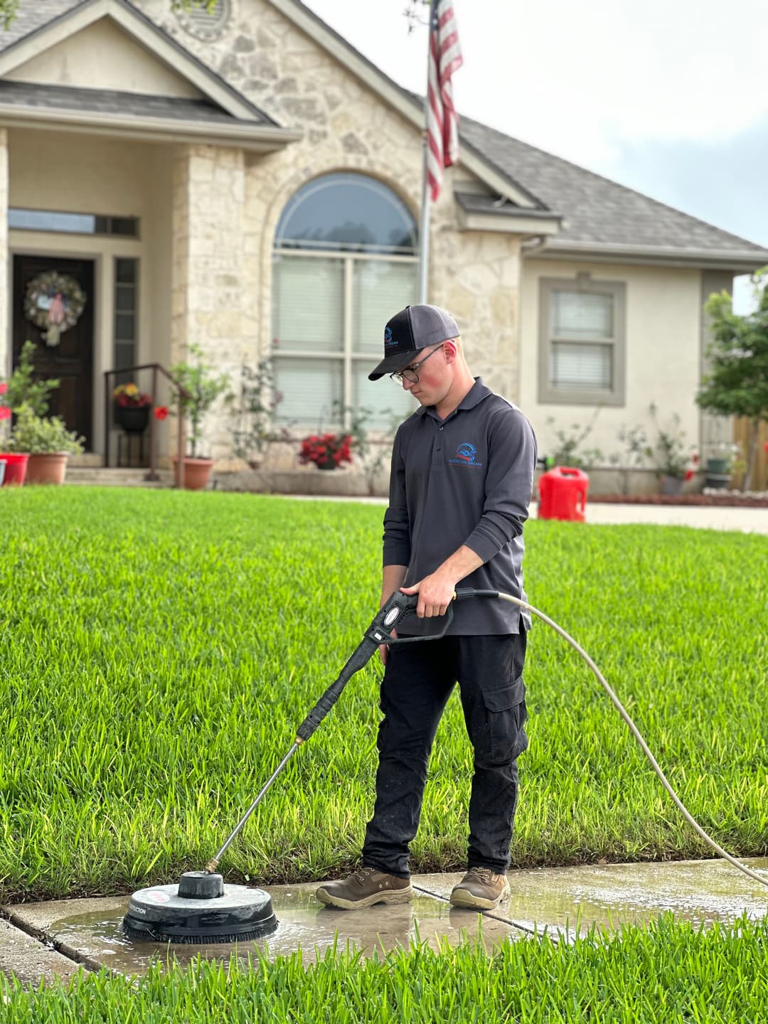 Man using a pressure washer on a patio with a well-maintained lawn and house in the background.
