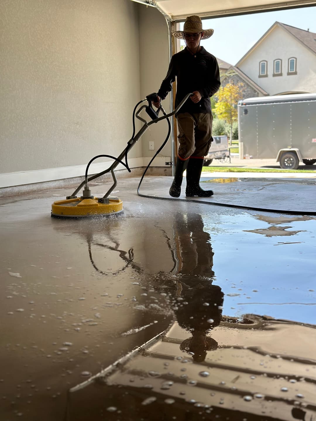 Person cleaning a garage floor with a pressure washer, reflecting water on the surface.