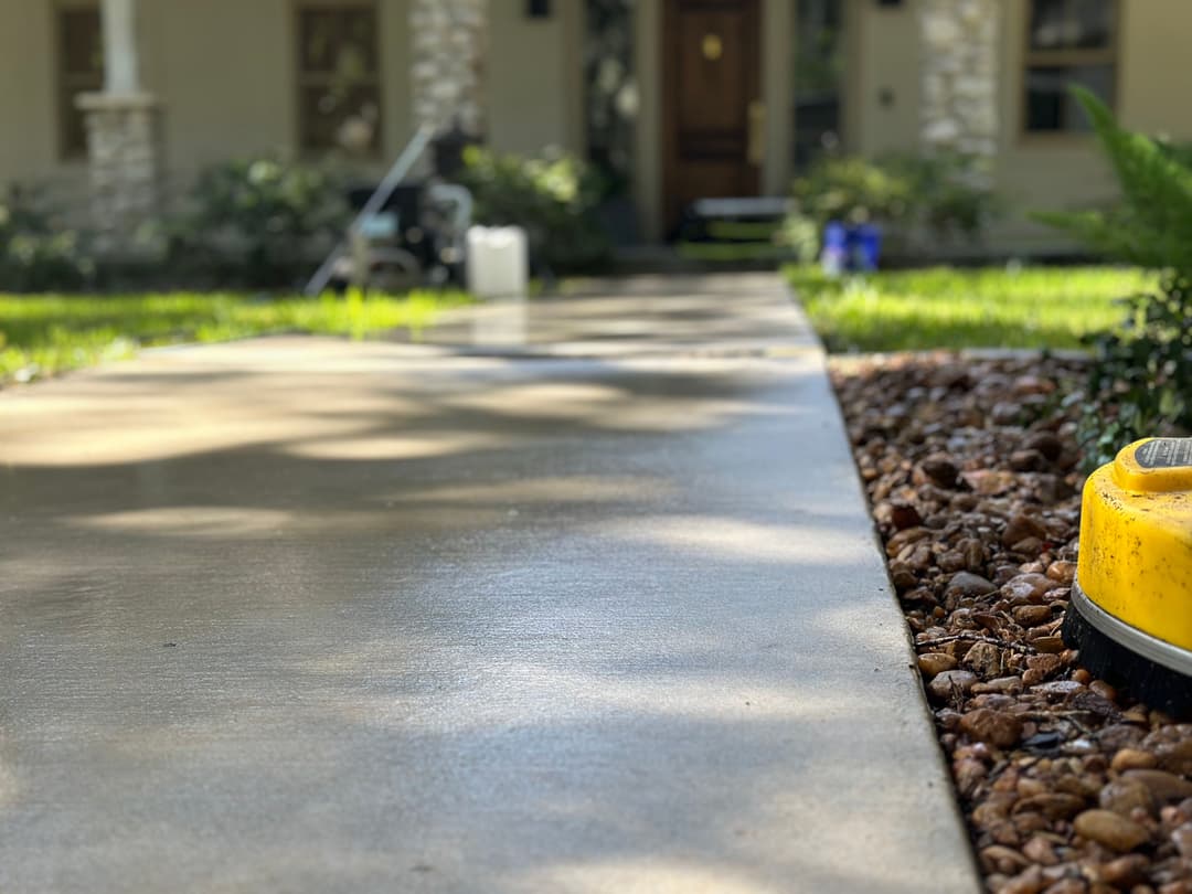 Clean concrete walkway leading to a home with decorative stone landscaping.
