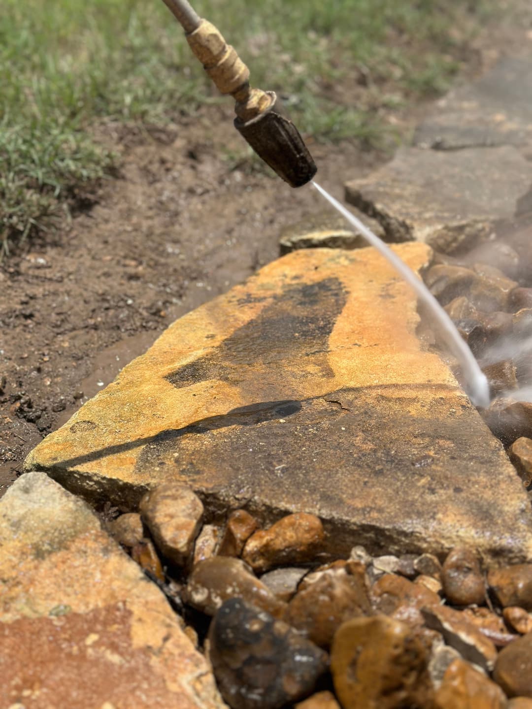 Pressurized water cleaning a stone path with pebbles, removing dirt and grime effectively.