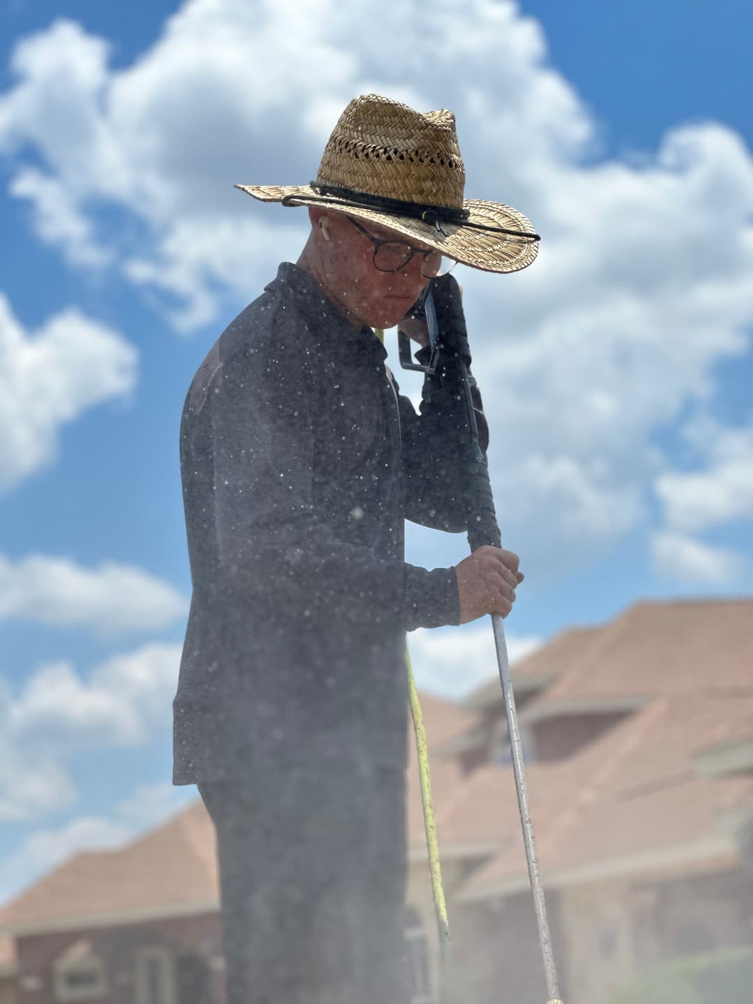 Person wearing a straw hat and glasses, holding a pole, working outdoors under a blue sky.