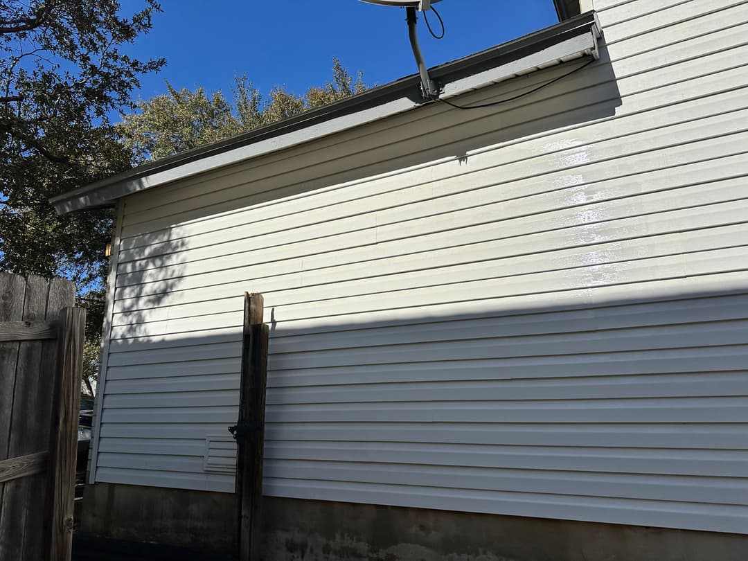 Well-maintained white siding on a house under a clear blue sky with shadows from trees.