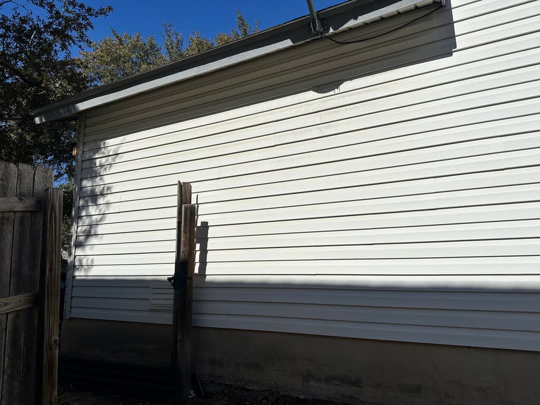 Side view of a white house with horizontal siding under a clear blue sky.