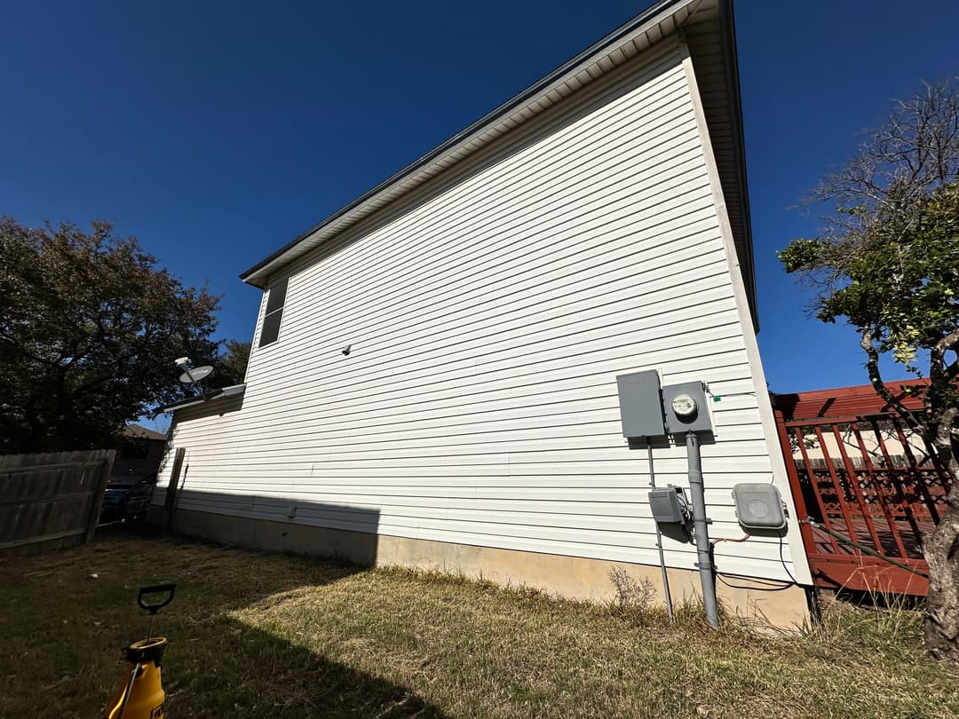 Side view of a home with siding, yard, and electrical meters under a clear blue sky.