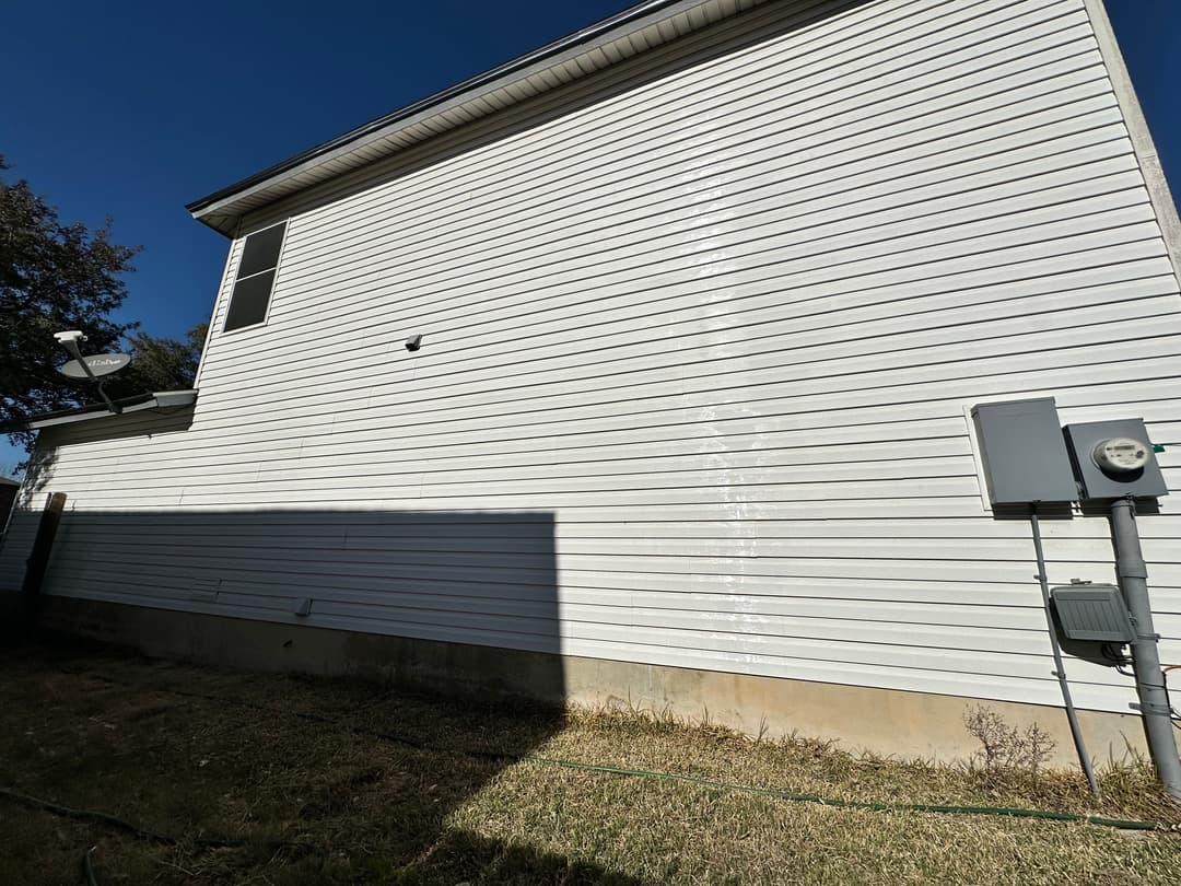 Side view of a house with white siding and utility meter, showcasing clear sky and grassy yard.