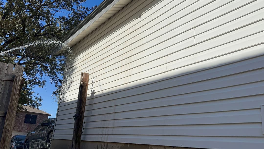 Water spray on a white vinyl siding house, showing maintenance or cleaning in progress.