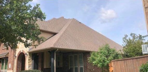 House exterior featuring a sloped roof, brick facade, and surrounding greenery.